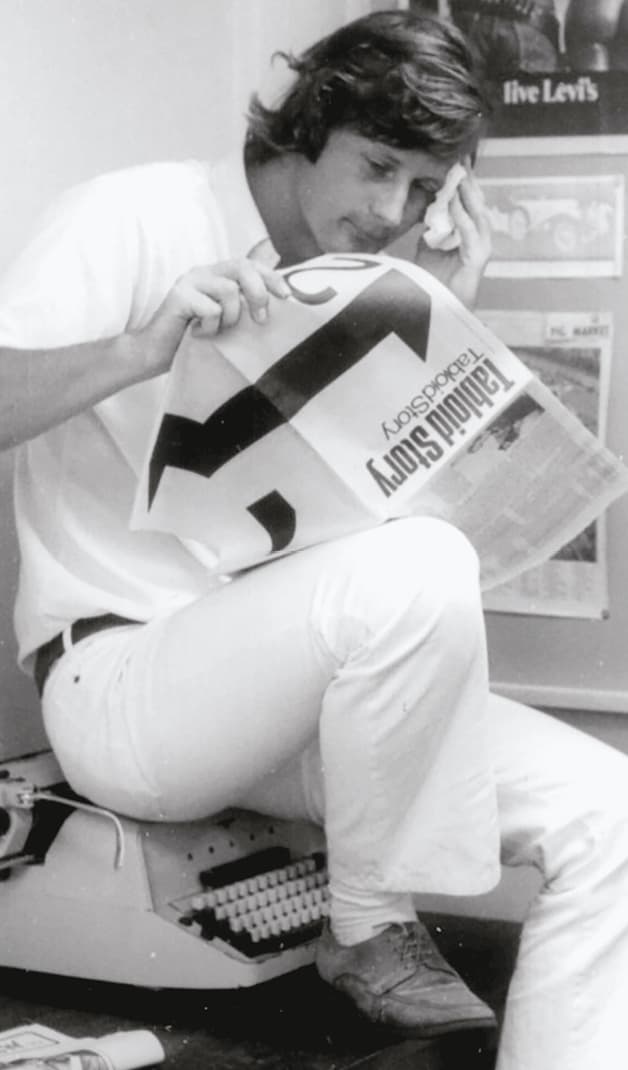 Craig Munro in an office, sitting atop a typewriter while reading.